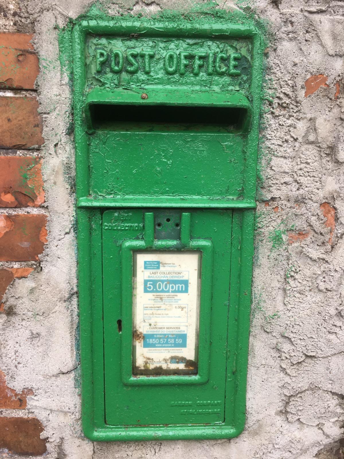 A green An Post postbox on an old Irish wall